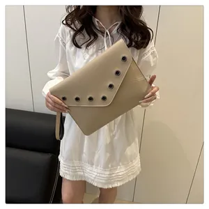 Detail of beige envelope clutch bag with metal eyelets and wrist strap shown by model