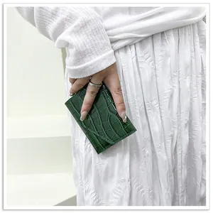 Detail of dark green crocodile texture patent leather envelope bag held by a model