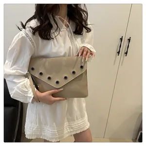 Detail of beige leather envelope clutch bag featuring rivet eyelets and wristlet strap