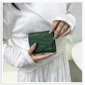 Detail of dark green crocodile texture envelope wallet held by a model for elegant style
