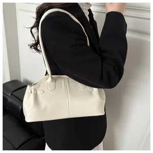Side view of a minimalist cream shoulder bag worn with a black blazer for work