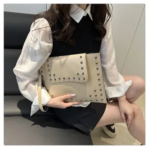 Detail of a beige envelope clutch bag with metal studs held by a model on a sofa