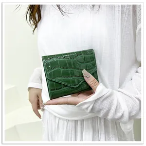 Detail of dark green crocodile embossed patent leather envelope wallet held by a model