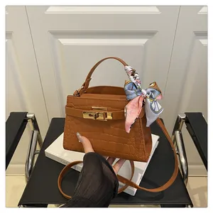 Detail of brown crocodile pattern handbag with silk scarf handle and golden metal lock