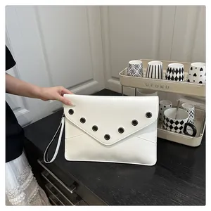 Detail of white PU leather envelope clutch with black grommets on a wooden surface