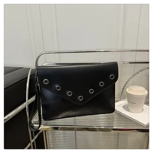 Detail of black envelope clutch featuring silver metal grommets and narrow wrist strap