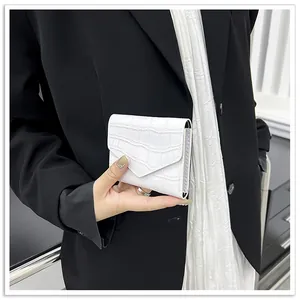 Close-up of white crocodile pattern envelope clutch held against a dark suit background