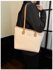 Sac fourre-tout chic en daim beige avec anses en cuir marron porté par un mannequin stylé
