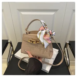 Detail of beige crocodile embossed handbag with gold turn-lock and elegant silk scarf