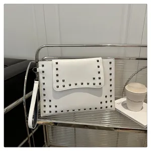 Detail of white leather envelope clutch featuring black studs on a silver metal shelf