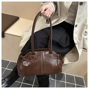 Detail of a dark brown glossy shoulder bag with vertical stitching and long handles