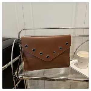 Close-up of brown leather envelope clutch bag with silver metal eyelets and wrist strap