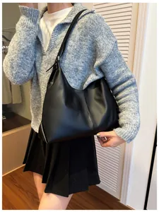 Detail of minimalist black matte leather hobo bag worn by model in a cozy indoor setting