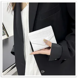 Detailed view of white crocodile pattern envelope clutch held by a fashion model