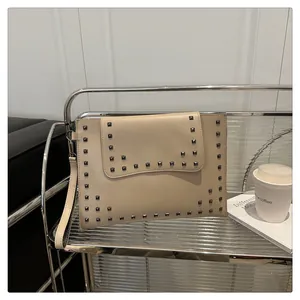 Detail of apricot envelope clutch with metallic square rivets on a modern silver cart