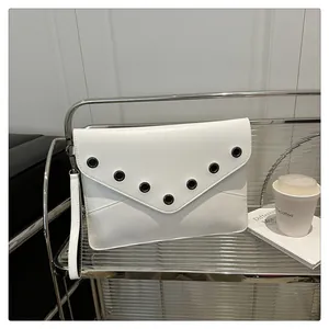 Close-up of white envelope clutch bag with black metal eyelets on a modern glass shelf