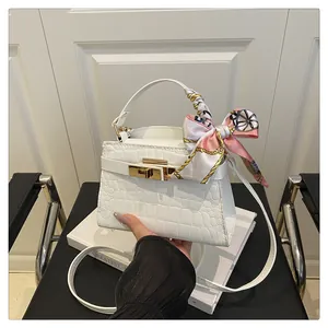 Detail of white crocodile-embossed handbag featuring a gold buckle and floral silk scarf