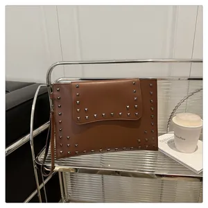 Detail of a brown leather envelope clutch bag featuring silver square studs on a metal rack