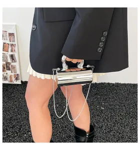 Detalle del bolso cilíndrico plateado con asa escultural y correa de cadena metálica