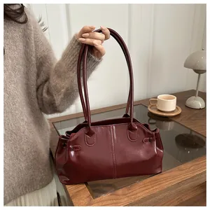 Detail of dark red glossy leather shoulder bag on a wooden table in a cozy setting