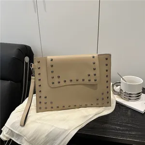 Elegant beige envelope clutch with silver square studs on white fabric background