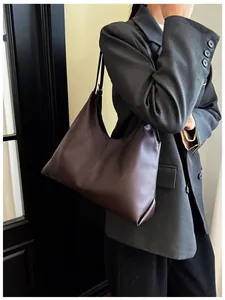 Detail of a large chocolate brown faux leather tote bag worn with a grey suit jacket