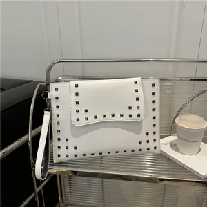Elegant white envelope clutch bag with black square studs and a wrist strap on a metal shelf