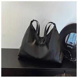 Detail of minimalist black leather tote bag with adjustable strap and matte finish texture