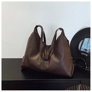 Detail of a large brown leather tote bag with vertical stitching and silver buckles