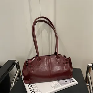 Minimalist deep red glossy shoulder bag with long handles placed on a black chair