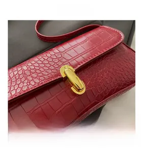 Close-up of burgundy crocodile pattern leather with golden metal clasp on handbag