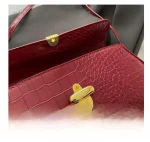 Detail of the golden pebble-shaped twist lock on a burgundy crocodile pattern handbag