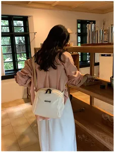 Detail of a white crossbody bag with adjustable strap worn by a model in a warm cafe
