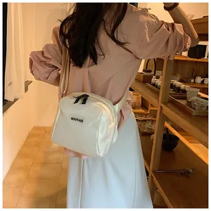 Detailed view of cream nylon crossbody bag with adjustable strap worn by a model