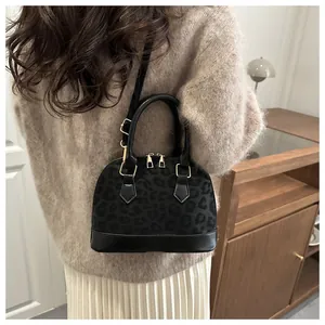 Detail of black leopard print shell bag featuring gold hardware and leather handles