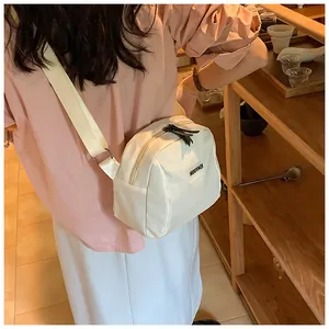 Crossbody ivory nylon bag shown on model featuring adjustable strap and black logo tag