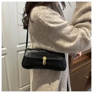 Close-up of black crocodile pattern leather baguette bag with a gold metal clasp detail