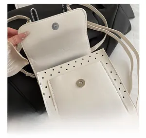 Detail of silver magnetic closure and black polka dot pattern on cream crossbody bag
