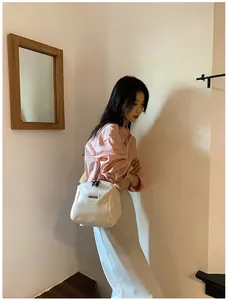 On-model shot of a white canvas crossbody bag with black bow and adjustable strap