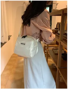 Model wearing a small cream PU leather crossbody bag with adjustable strap and logo detail