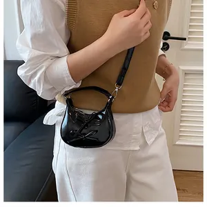 Kleine schwarze Lackleder Umhängetasche mit Schleife, getragen von einem Modell