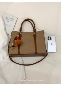 Detail of a brown woven tote bag with leather trim and decorative plush ball charm