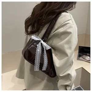 Deep brown patent leather bag with white lace bow shown on a shoulder of a model
