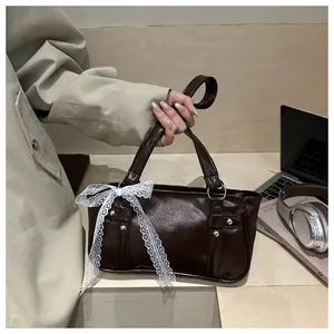 Detail of dark brown glossy leather handbag with lace bow and silver stud accents