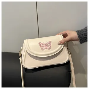 Détail d'un sac bandoulière crème avec broderie papillon rose et accessoires dorés