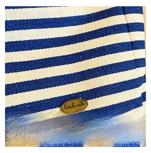 Macro shot of blue striped canvas fabric texture with an oval bronze handmade metal plate