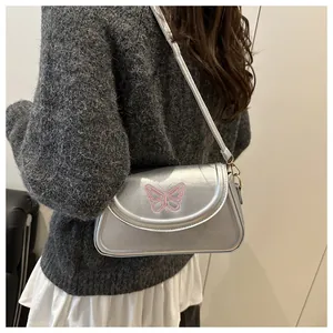 Détail d'un sac argenté avec broderie papillon rose et crochets métalliques dorés élégants