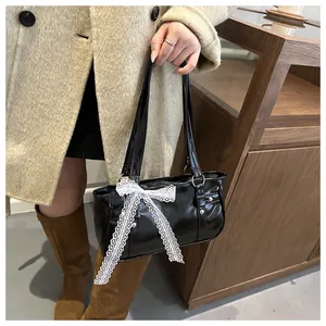 Detail of black glossy handbag with a large white lace bow and twin leather straps