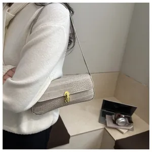 Detail view of cream crocodile embossed underarm bag with gold metal lock on a female model