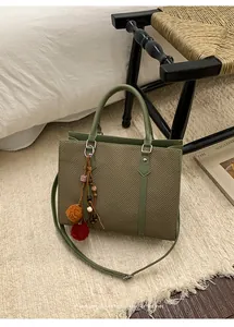 Detailed shot of an olive green woven shoulder bag with a colorful boho pom-pom charm